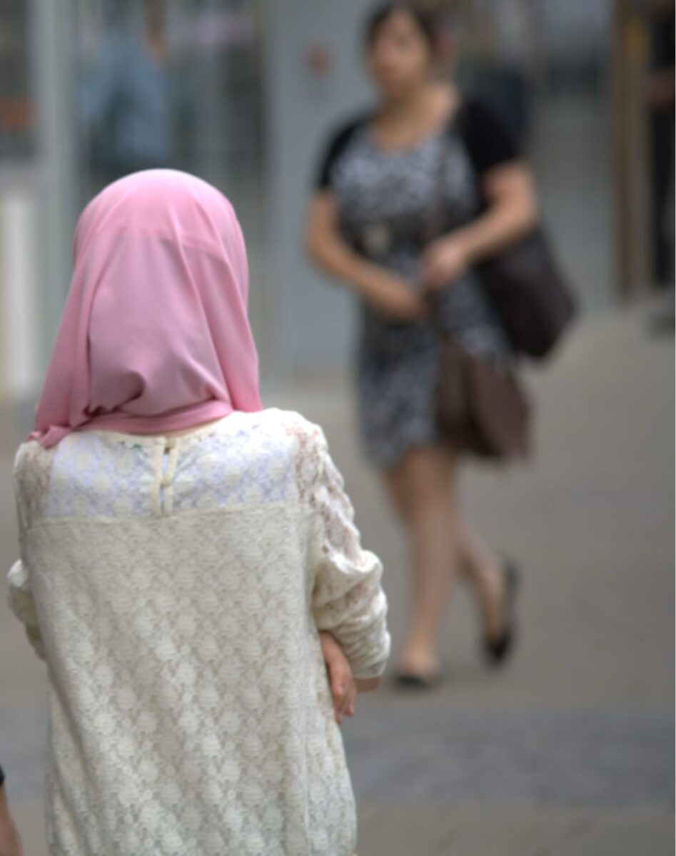 Ein Mädchen von hinten mit weißem Pulli und rosa Kopftuch (Hijab).